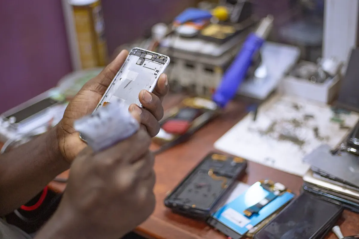 A repair technician holding an opened phone frame over a bench with screens and tools